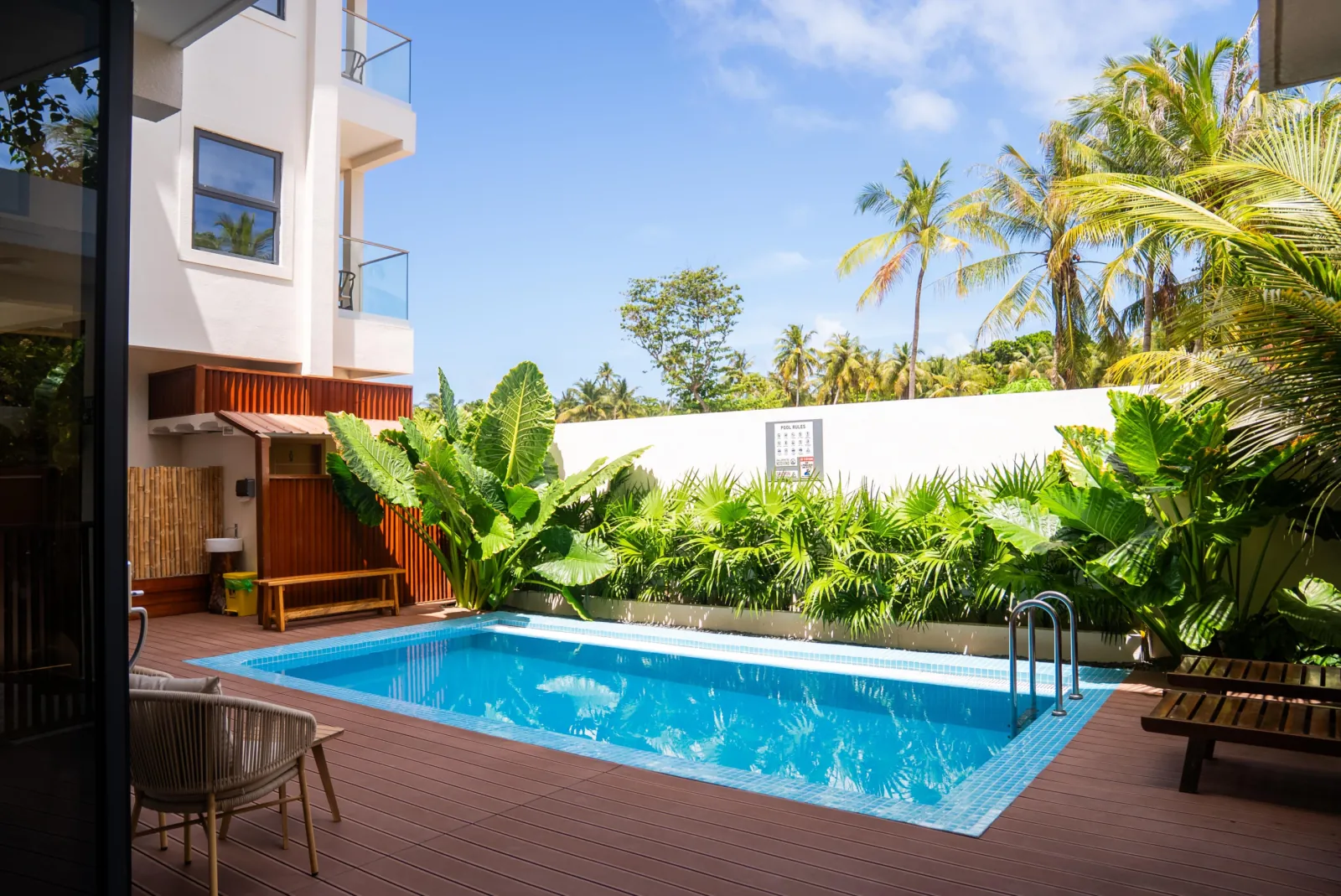 AIRE Dharavandhoo's turquoise tiled pool on composite decking with a planted border, palms behind and the white guesthouse building at left