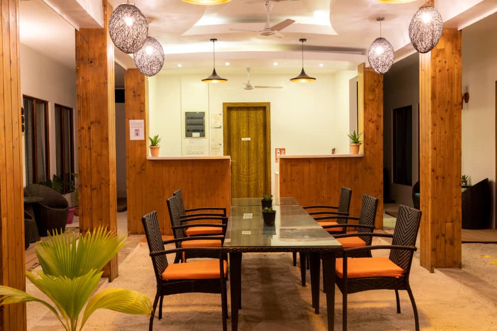 LVIS Village's sand-floored courtyard lounge at night, with timber columns, wicker pendant lamps and a communal glass dining table